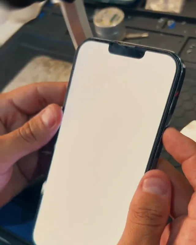 Técnico segurando um iPhone com a tela nova acesa em branco, no teste de imagem e toque antes da entrega