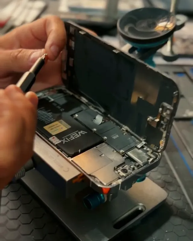 iPhone aberto na bancada da Repara Cell BH, com a tela levantada e o técnico soltando os parafusos durante a troca de tela